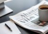 Newspaper on a modern desk with coffee and notepad.